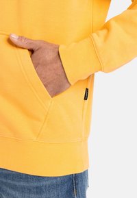 Yellow cotton sweatshirt with a kangaroo pocket, ribbed cuffs, and a hem. Features a visible brand tag on the pocket.