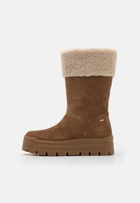 Brun mockasinistövel med tjock sula, med en beige fuskpälsfåll och geometrisk prägling på ovandelen. Rundad tådesign.