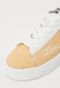 Light-colored sneaker with woven texture, white leather accents, and thick white laces. "Love Moschino" is embroidered in white on the side.