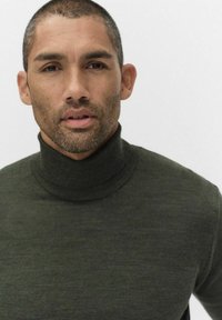 Donkergroen coltrui van zacht materiaal, met een aansluitende hoge kraag en een gladde, geribbelde structuur.