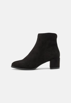Sort ruskind ankle støvle med rundet tå og blokhæl på en ensartet lys baggrund.