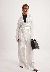 Valge tekstureeritud kimono-stiilis jakk, mis on seotud vöödiga, koos laia säärega valgete pükstega. Must topp ja käekott täiustavad komplekti.