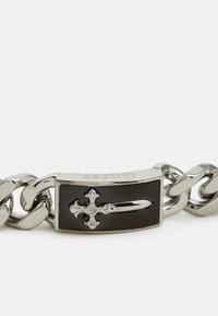 Náhrdelník ze stříbrného tónovaného kovu s tlustými články, s obdélníkovým černým emblémem s designem stříbrného kříže a značkovým vyrytím.