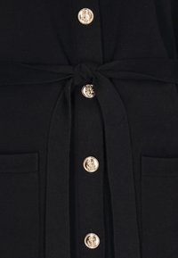 Czarny ubiór z paskiem zawiązanym w talii, z złotymi guzikami z tłoczonym wzorem kotwicy i dwoma przednimi kieszeniami.