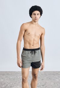 Khaki és fekete fürdőnadrágok, húzózsinóros derékrésszel, elől logóval és sima, vízlepergető textúrával.