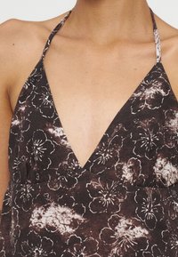 Gros plan d'une personne portant un top dos nu foncé avec des motifs floraux blancs et marron et un décolleté en V profond.