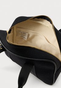 Μαύρη υφασμάτινη τσάντα ώμου με ανοιχτό χρυσό φερμουάρ, μπεζ εσωτερική επένδυση και ραμμένη ετικέτα μάρκας στην εσωτερική τσέπη.