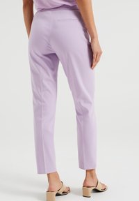 Levandulové kalhoty s přiléhavým střihem, vyrobené z hladké tkaniny, mají zadní kapsu a rovné nohavice, stylizované s béžovými sandály na podpatku.
