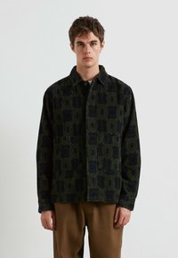 Giacca in corduroy verde scuro con un motivo geometrico, dotata di due tasche frontali, chiusura con bottoni e colletto a punta.