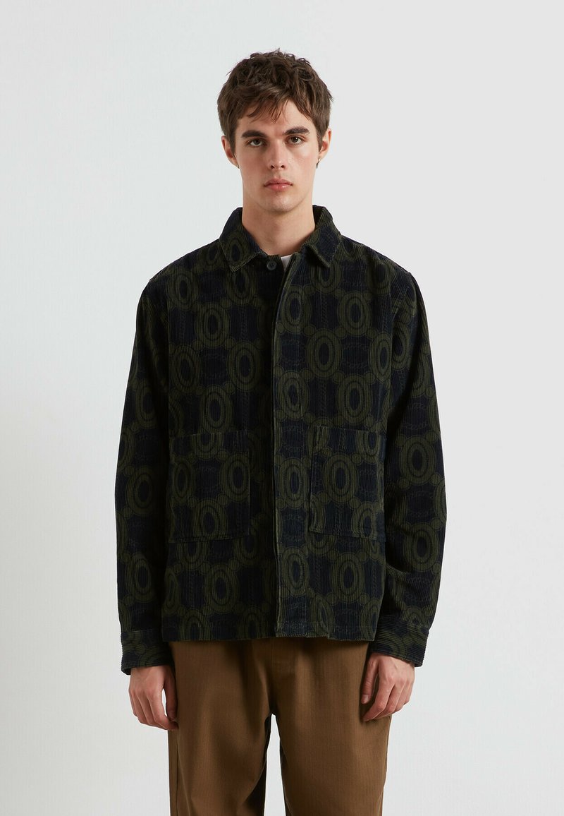 Giacca in corduroy verde scuro con un motivo geometrico, dotata di due tasche frontali, chiusura con bottoni e colletto a punta.
