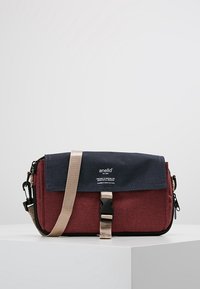 Röd och marinblå väska med klaffstängning, justerbar beige rem och logotypdetalj. Texturerat tyg med rektangulär form och dragkedjeficka.