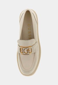 Beige leather loafer with a rounded toe, decorative stitching, and a gold buckle featuring the letter "G." Smooth texture, minimal design.