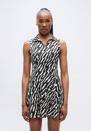 Rochie alb-negru fără mâneci, cu guler, având un model în zigzag. Fustă evazată și corset mulat cu textură netedă.