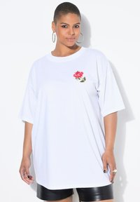 Camiseta blanca de gran tamaño con bordado de una rosa roja en el lado izquierdo del pecho. Material de algodón suave, con mangas cortas y un corte relajado.