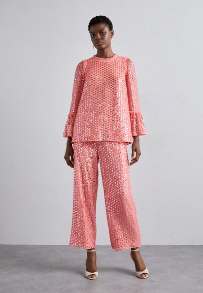 Two-piece outfit in light pink with large sequins. Top features flared sleeves; trousers are wide-legged. Smooth texture with shiny accents.