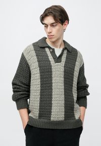 Texturált kötött pulóver gallérral, sötétszürke és világosszürke függőleges csíkokkal. Két gombos díszítést és bordázott mandzsettákat tartalmaz.