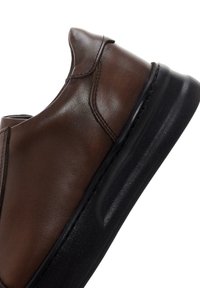 Zapato de cuero marrón sin cordones, con un acabado suave, puntera ligeramente redondeada y suela de goma negra para mayor tracción. Sin cordones ni herrajes visibles.