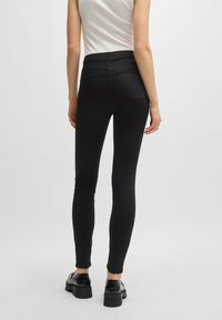 Jeans skinny neri con vita alta, tasche posteriori e una texture liscia. Abbinati a scarpe con plateau nere.