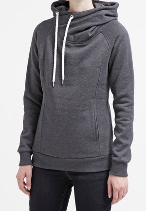 Femme portant un sweat à capuche gris foncé avec des cordons blancs, des manches longues et des poches avant, assorti à un pantalon noir.