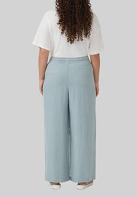 Pantalons larges bleu clair avec une taille élastique, fabriqués dans un tissu doux et texturé, associés à une chemise blanche basique à manches courtes.