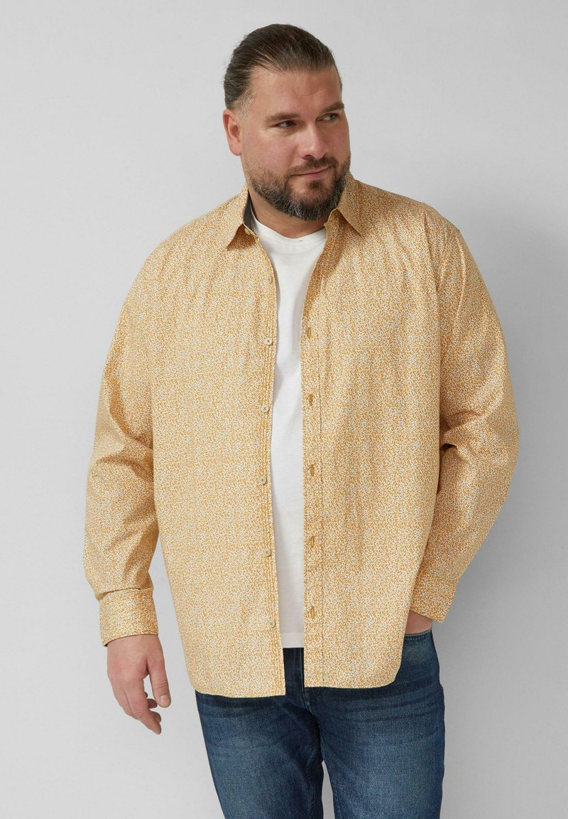 Koszula na guziki w jasnym żółtym kolorze z drobnymi, białymi kwiatowymi wzorami. Posiada długie rękawy, luźny krój i klasyczny kołnierzyk.