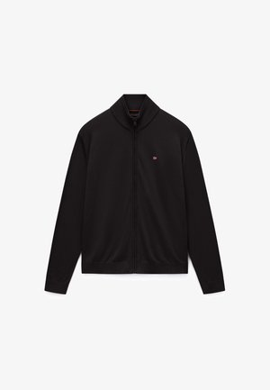 Suéter negro con cremallera, cuello y puños acanalados, con un pequeño emblema de bandera roja y blanca en el pecho izquierdo.