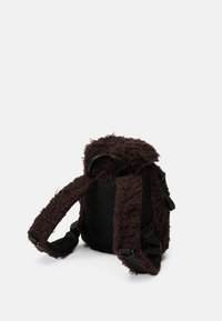 Mochila castanha com textura peluda, alças ajustáveis, painéis laterais em malha e formato arredondado. Apresenta uma aparência suave e acolhedora.