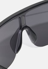 Sauleņa brilles ar melnu apmali un tumšiem lēcas, ar elegantu, modernu dizainu un izteiksmīgu izgriezuma tiltu, kas uzlabo piemērotību.