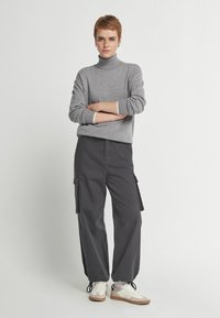 Grå polo-neck tröja, avslappnad passform; svarta cargobyxor med sidofickor; vita sneakers med beiga detaljer; slät yta.