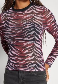 Kvinde iført en tætsiddende langærmet mesh-top med røde, sorte og pink zebra-striber samt teksten "Juicy Couture", kombineret med sorte jeans.