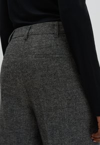 Grijze gemêleerde broek met een nauwsluitende pasvorm, voorzien van een rechte snit, een tailleband en subtiele zakdetails. De stof heeft een geweven patroon.