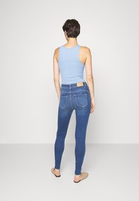 Top azul em tecido fluido com um corte ajustado, combinado com jeans skinny de cintura alta em azul escuro, com bolsos traseiros e um rótulo de couro na cintura.