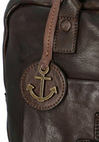 Bolso de cuero marrón con una etiqueta redonda de ancla, que presenta una textura suave, detalles cosidos y un cierre de bronce.