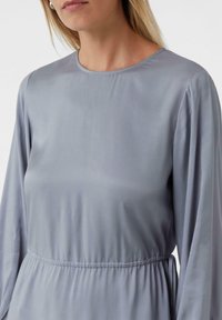 Szara sukienka z długim rękawem, wykonana z gładkiego materiału, z okrągłym dekoltem i detalem elastycznej talii, charakteryzująca się subtelną teksturą i swobodną sylwetką.