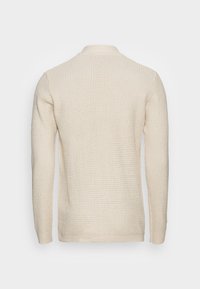 Stickad tröja i ljusbeige med ett strukturerat mönster, rund halsringning och ribbade manschetter. Enfärgad rygg utan utsmyckningar.