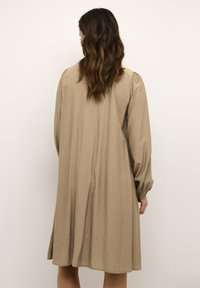 Dlouhé šaty khaki barvy z jemného materiálu, s žebrovanou texturou a nabíranými rukávy. Kousek má volný střih a sahá těsně nad kolena.