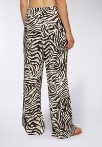 Pantaloni a gamba larga con stampa zebra marrone e crema, realizzati in un tessuto morbido; presentano un elastico in vita e una vestibilità rilassata.