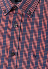 Plaid shirt featuring blue and orange hues, button-down collar, chest pocket with logo embroidery, and textured fabric.
