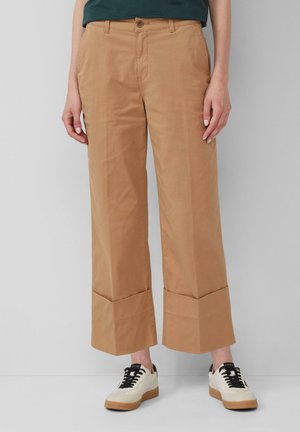 Pantaloni larghi color khaki realizzati in cotone, con chiusura a pulsante, tasche frontali e orlo piegato. Abbinati a sneaker color crema.