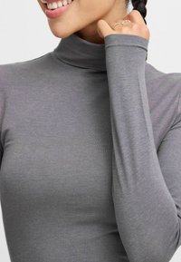 Maglia a maniche lunghe grigia con collo alto realizzata in un morbido e elastico tessuto dal design aderente, con colletto alto e maniche lunghe.