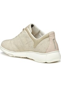 Zapatilla de color beige claro con una parte superior de tela texturizada, diseño de cordones elásticos y suela blanca acolchada. Presenta un detalle en el talón de cuero suave.