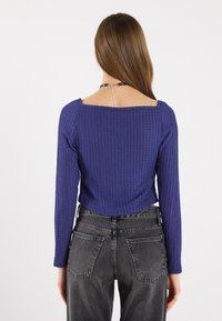 Maglietta a maniche lunghe viola con scollatura quadrata, lunghezza cropped e tessuto texturizzato, abbinata a jeans neri in denim a vita alta.