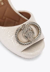 Scarpa peep-toe in pelle color avorio con una fibbia decorata in oro e strass trasparenti. Parte superiore texturizzata e interno liscio.