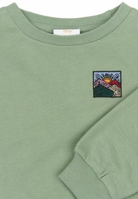 Svetlozelena sweatshirt z rebrastim ovratnikom in manšetami. Ima kvadratni vezen izraz, ki prikazuje gore, sonce in modro nebo.