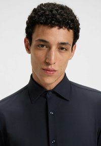 Camicia blu navy con tessuto texturizzato, colletto a punta e bottoni scuri. Primo piano sulla camicia, enfatizzando il suo design e il colore.