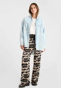Lichtblauwe oversized spijkerblouse, wit T-shirt, brede zwart-beige geprinte broek en zwarte platform sandalen.