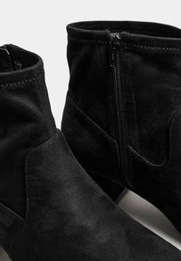 Botines de ante negros con cremallera lateral, textura suave, detalles de costura sutiles y un tacón afilado para una silueta elegante.