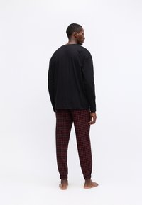 Schwarzes Langarmshirt kombiniert mit rot-schwarz karierter Hose, die einen elastischen Bund und gerippte Bündchen hat.