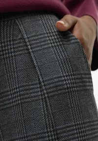 Grå rutiga byxor med ett klassiskt hundtandmönster och en strukturerad yta; ficka synlig. Tillverkade av vävt tyg, något avslappnad passform.