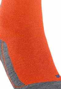 Helle orange strukturierte Socke mit einem grauen Akzentbereich an der Ferse, die feine Rippungen aufweist und ein kleines blaues Logo an der Seite hat.